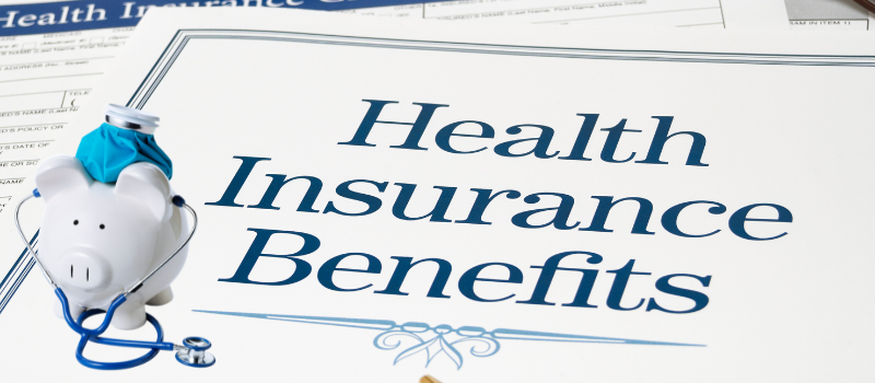 Alcancía con estetoscopio junto a documentos de Health Insurance Benefits, representando el aumento en el costo del seguro médico en 2026